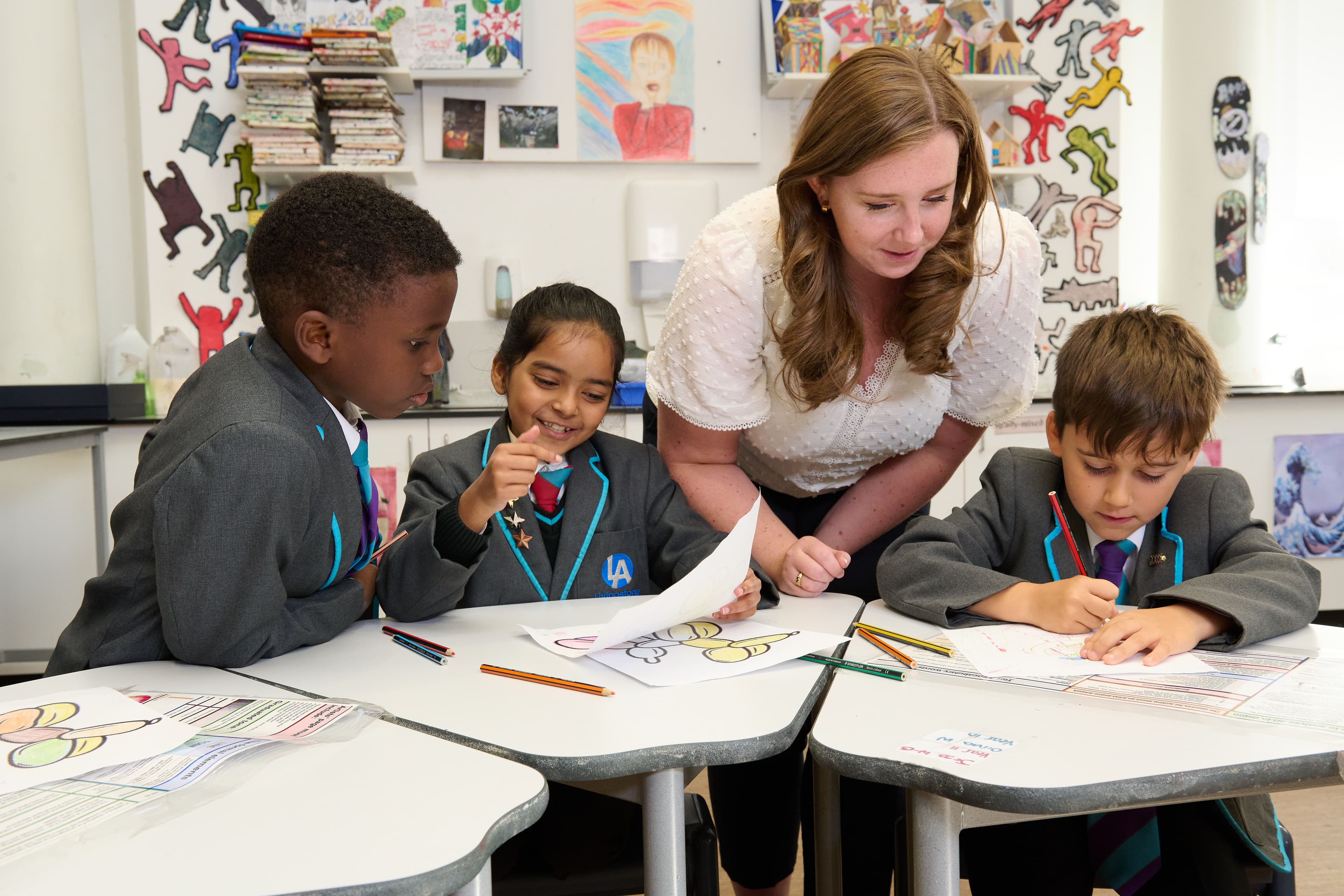 Teacher helps 3 young children with their drawings in class