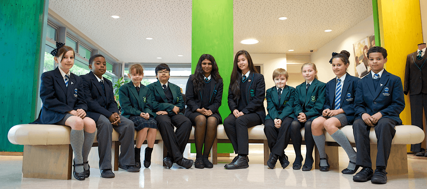Ten students pose for a picture, sitting on a bench in the school reception.